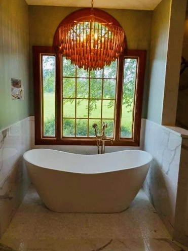 Freestanding white bathtub under a window with a view, and a wooden chandelier.
