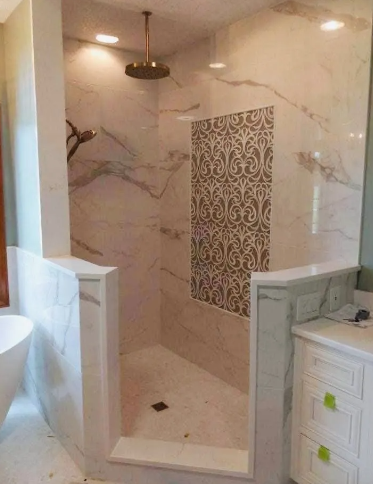 Marble-tiled walk-in shower with decorative mosaic accent wall, bronze shower fixtures, and white cabinetry.