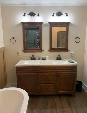 Bathroom with double vanity, mirrors, and sconces. Wooden cabinetry and light-colored walls.