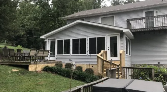 A house with a screened-in porch and deck, backyard with greenery.