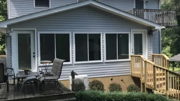 Back of a light blue house with a sunroom, deck, and wooden staircase.