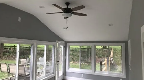Sunroom with gray walls, white ceiling, glass windows and door, ceiling fan, and outdoor view.