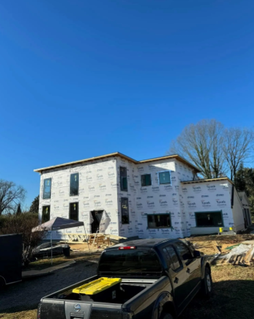 Two-story house under construction, wrapped in white material, with a black pickup truck in the foreground.
