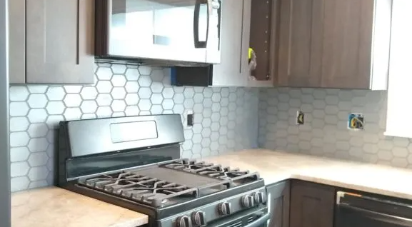 Kitchen with dark cabinets, hexagon tile backsplash, and stainless steel appliances.