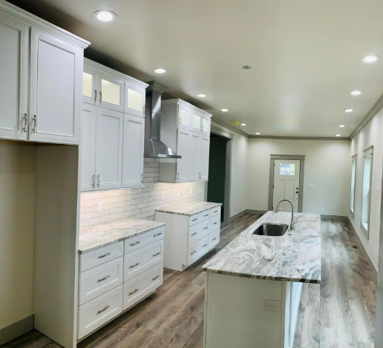 White kitchen with island, countertops, cabinets, stainless steel range hood, and wood-look flooring.