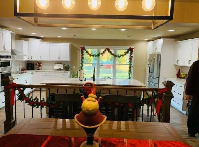 A decorated kitchen with a large island, white cabinets, and Christmas garland.