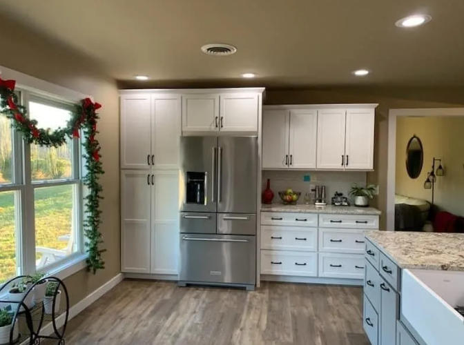White kitchen with stainless steel refrigerator and cabinets, a window with a garland, and gray floors.
