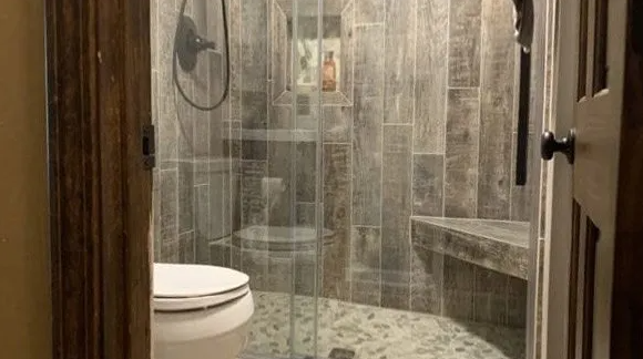 Bathroom with shower and toilet visible through open doorway. Stone tile walls, glass shower door.