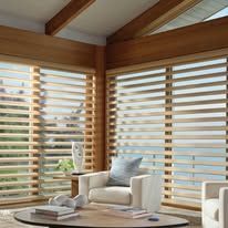 A living room with a chair , table , and blinds on the windows.