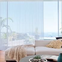 A living room with a couch , table , and window with vertical blinds.