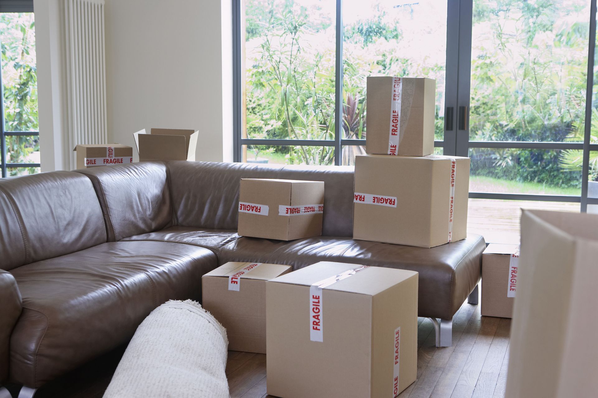 Living room with brown leather sectional sofa and cardboard boxes, some labeled 