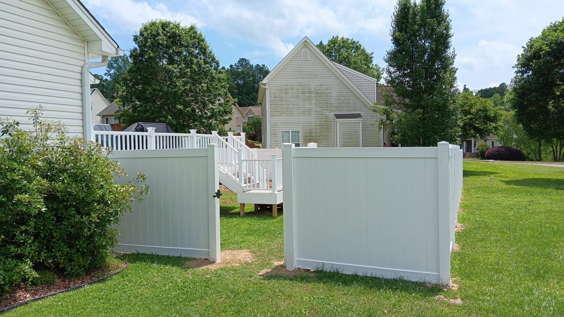 A white fence surrounds a lush green yard in front of a house.