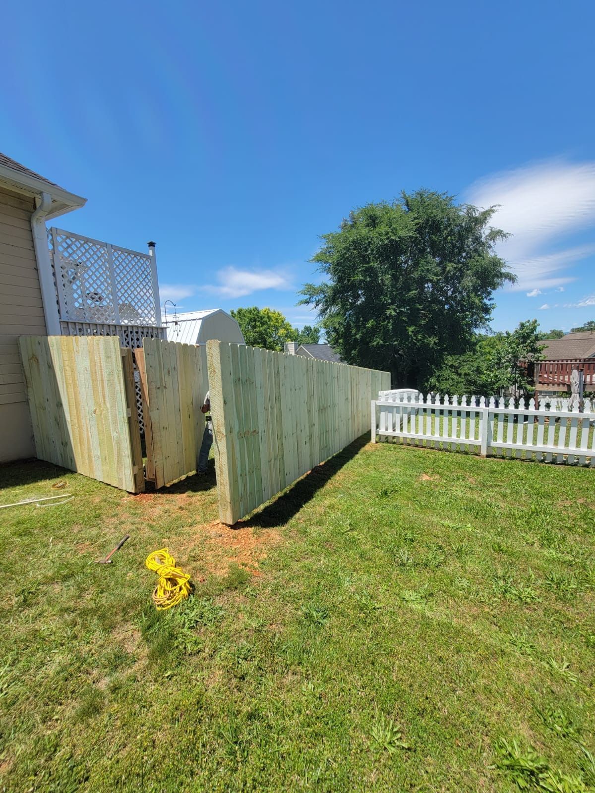 A wooden fence is sitting in the middle of a lush green yard next to a white picket fence.