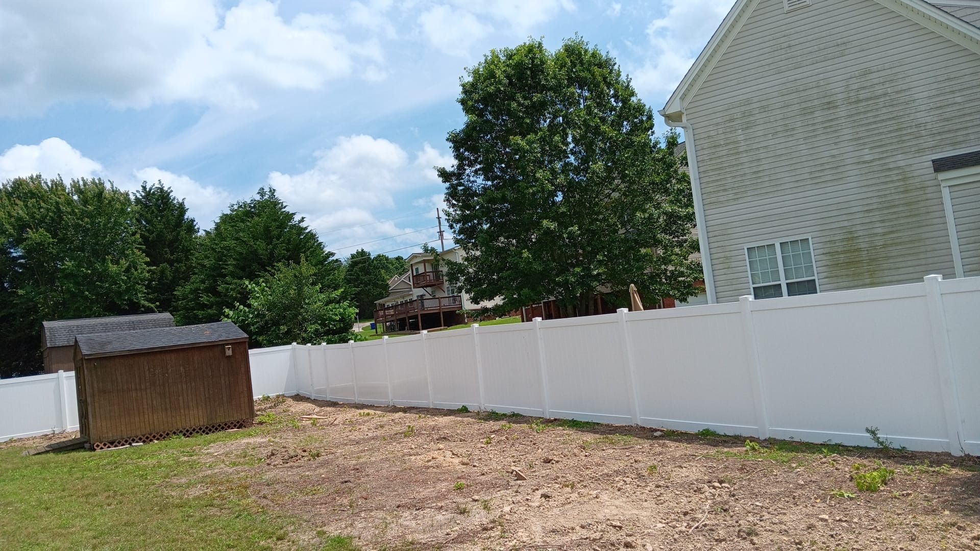 A white fence surrounds a yard with a shed and a house in the background.