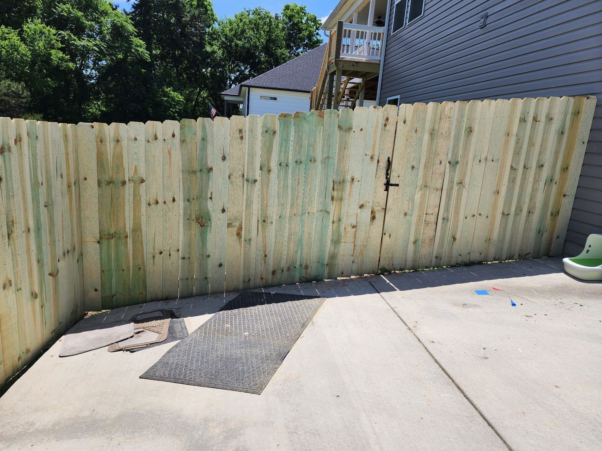 A wooden fence surrounds a concrete patio in front of a house.