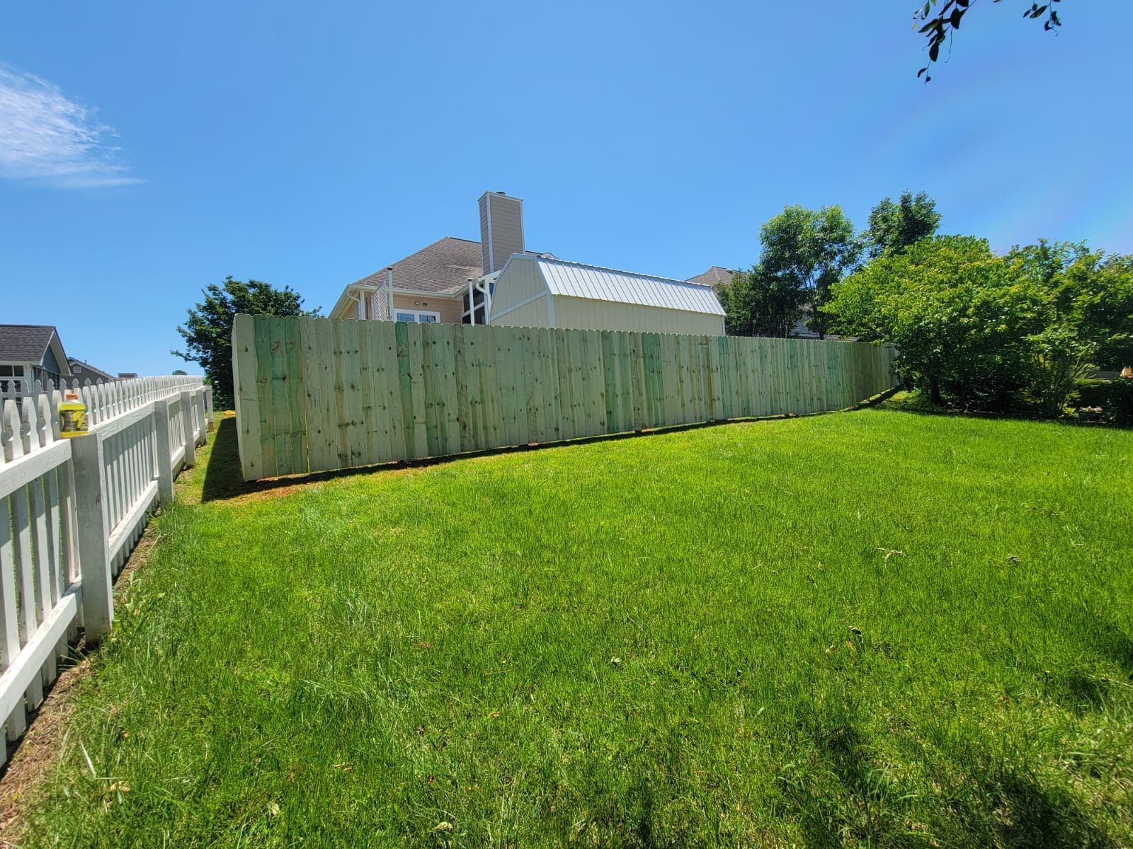 A wooden fence surrounds a lush green lawn in front of a house.