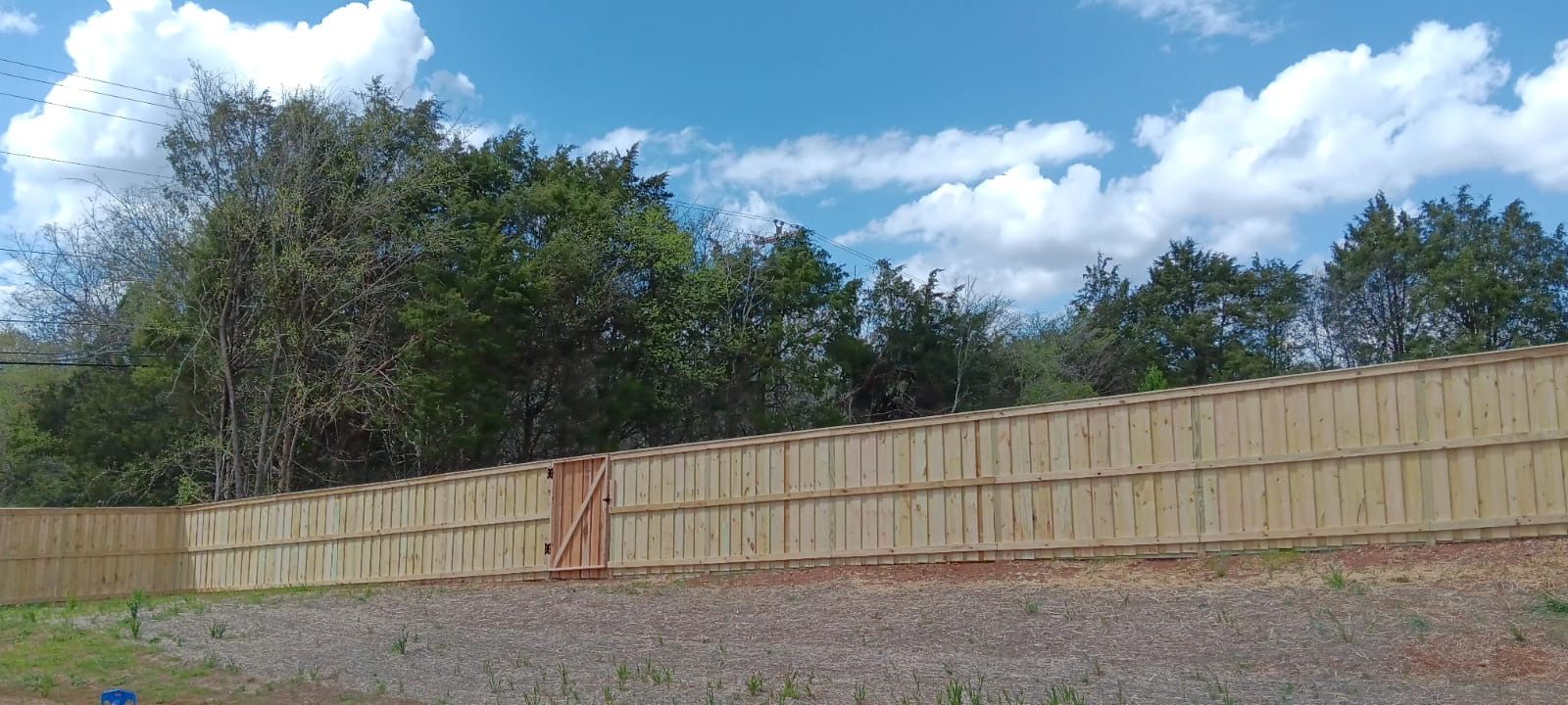 A wooden fence is surrounded by trees and gravel on a sunny day.