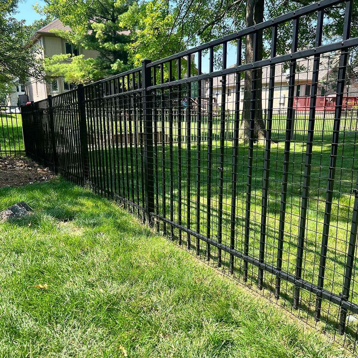 A black metal fence surrounds a lush green yard.
