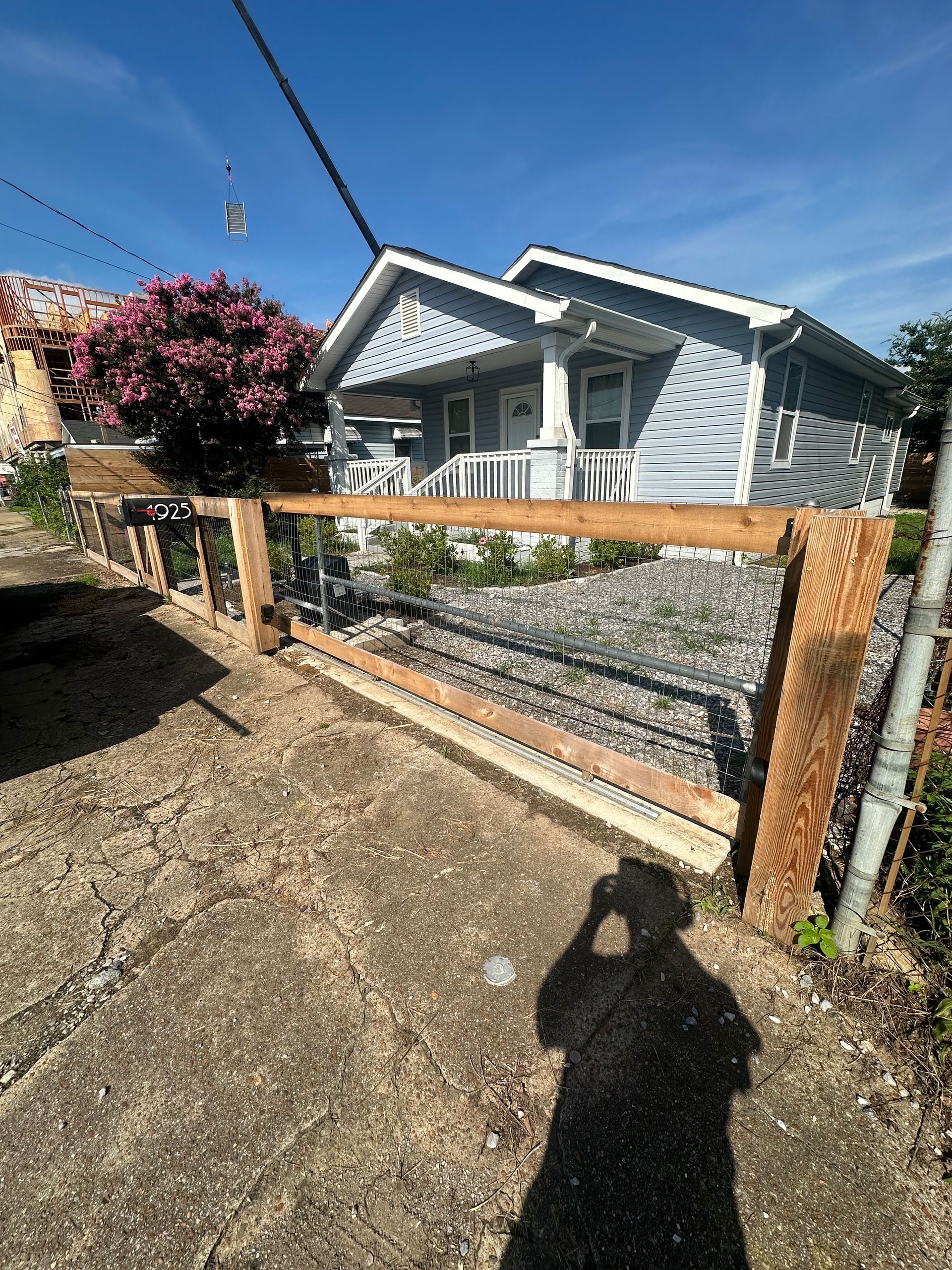A person is taking a picture of a house with a wooden fence in front of it.
