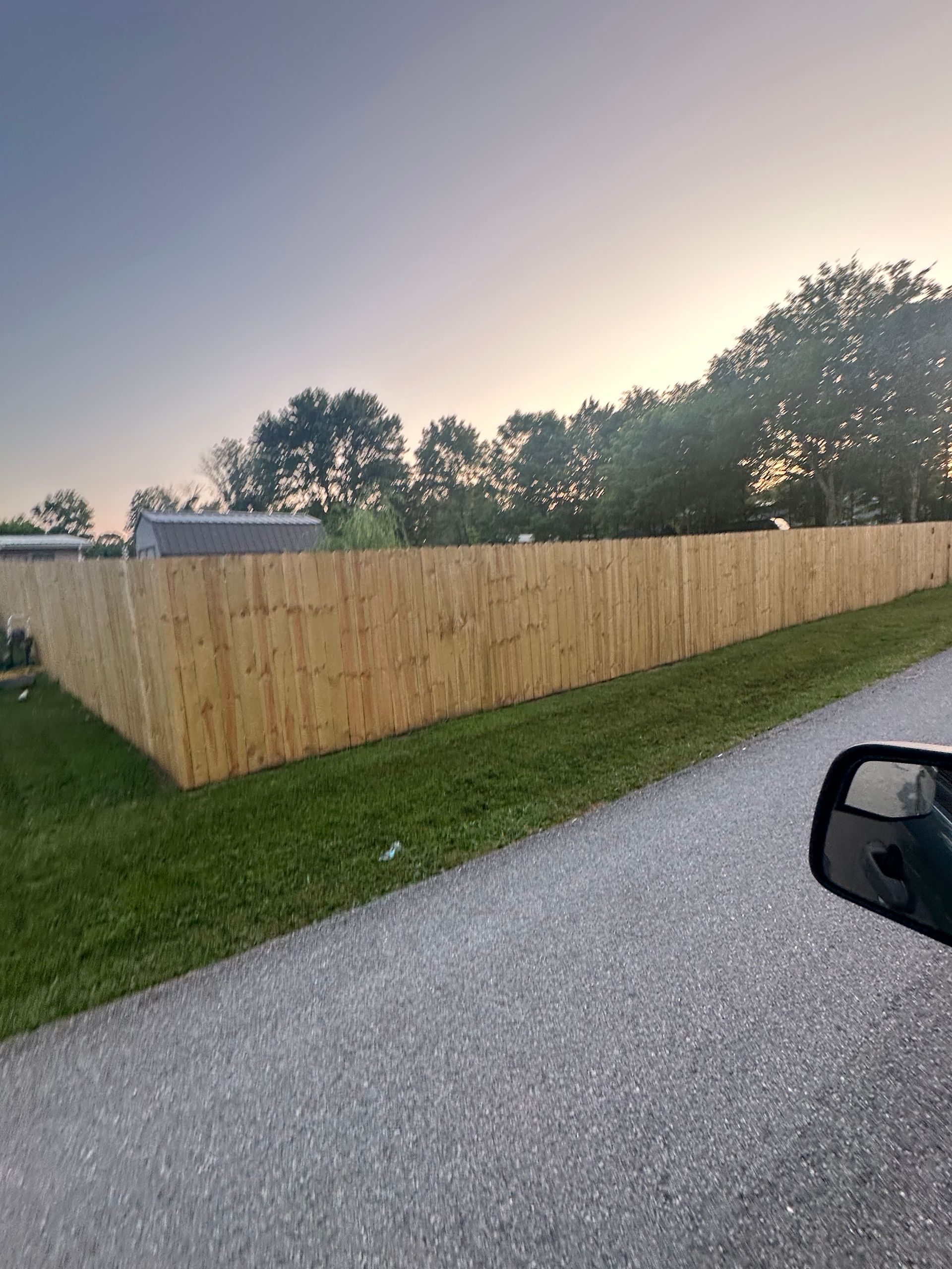 A car is driving down a gravel road next to a wooden fence.