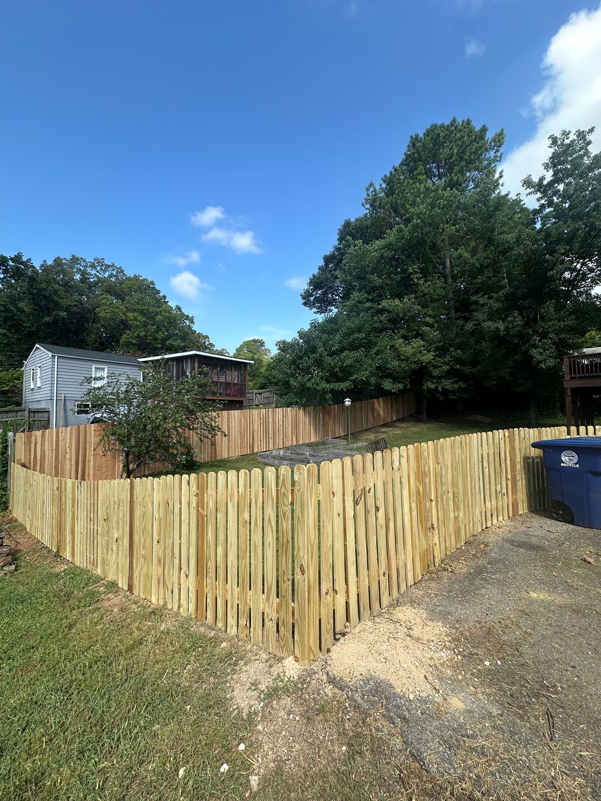 A wooden fence is surrounding a yard with a house in the background.