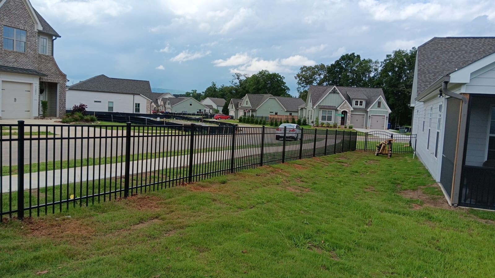 A black fence surrounds a lush green yard in a residential neighborhood.