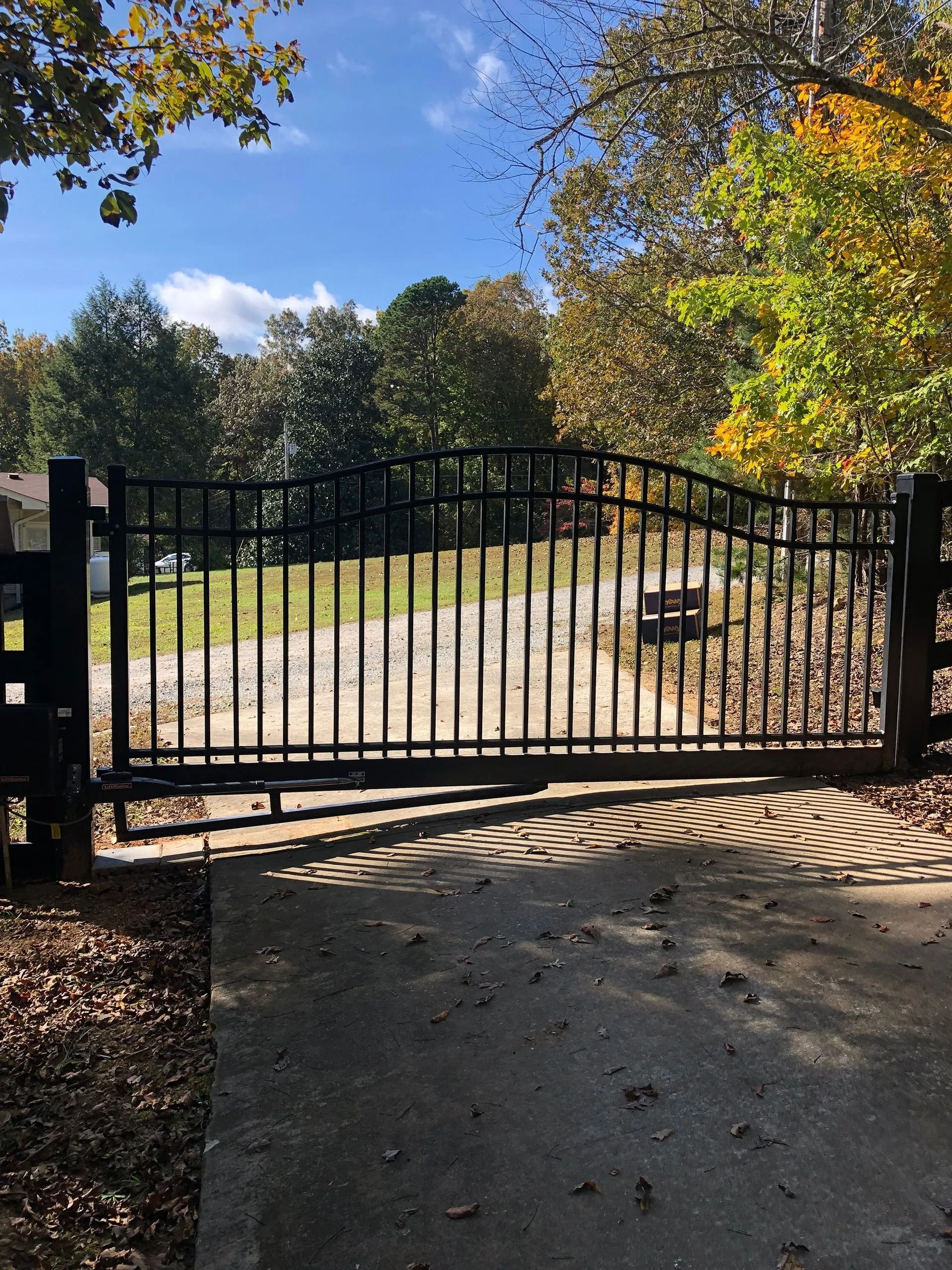 A black gate is open to a driveway with trees in the background