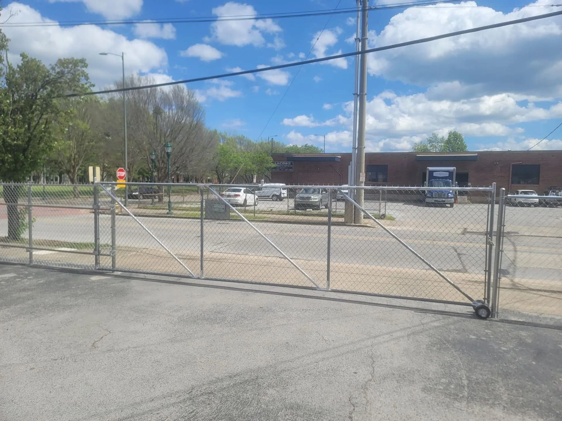 A chain link fence surrounds a parking lot with a building in the background.