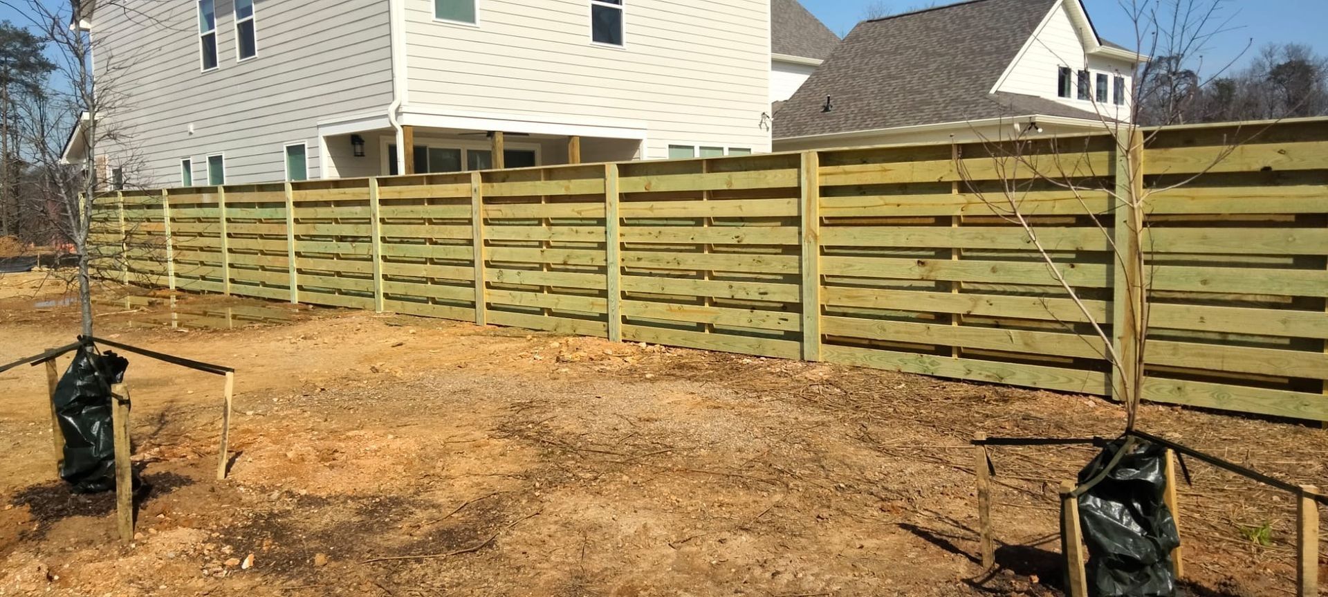A wooden fence surrounds a yard with a house in the background.
