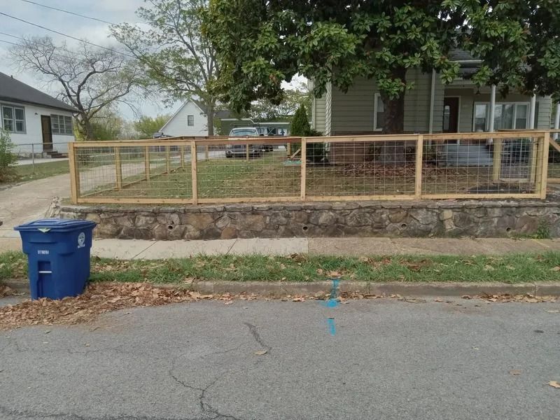 A blue trash can sits next to a wooden fence