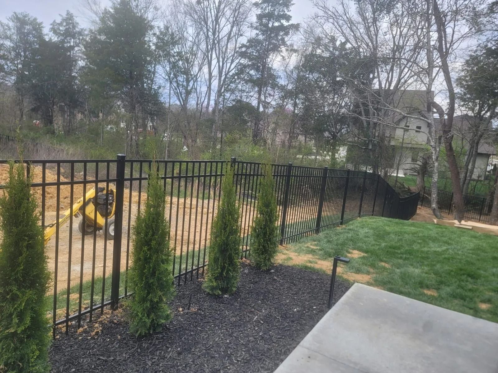 A black metal fence surrounds a lush green yard with trees.