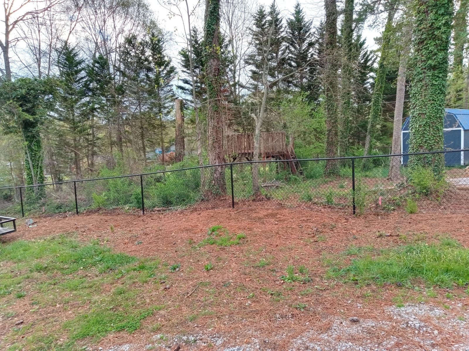 There is a fence in the middle of a field with trees in the background.