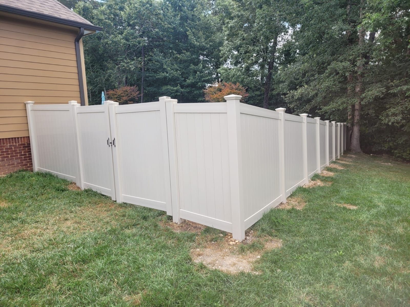 A white vinyl fence with a gate in the backyard of a house.