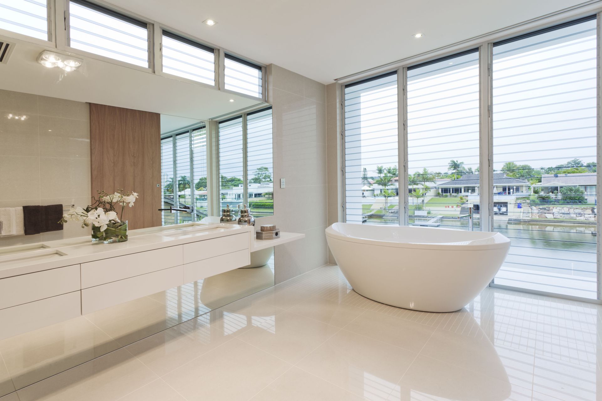 Spacious modern bathroom with a free-standing tub, large windows with a view, white surfaces, and glossy floors.
