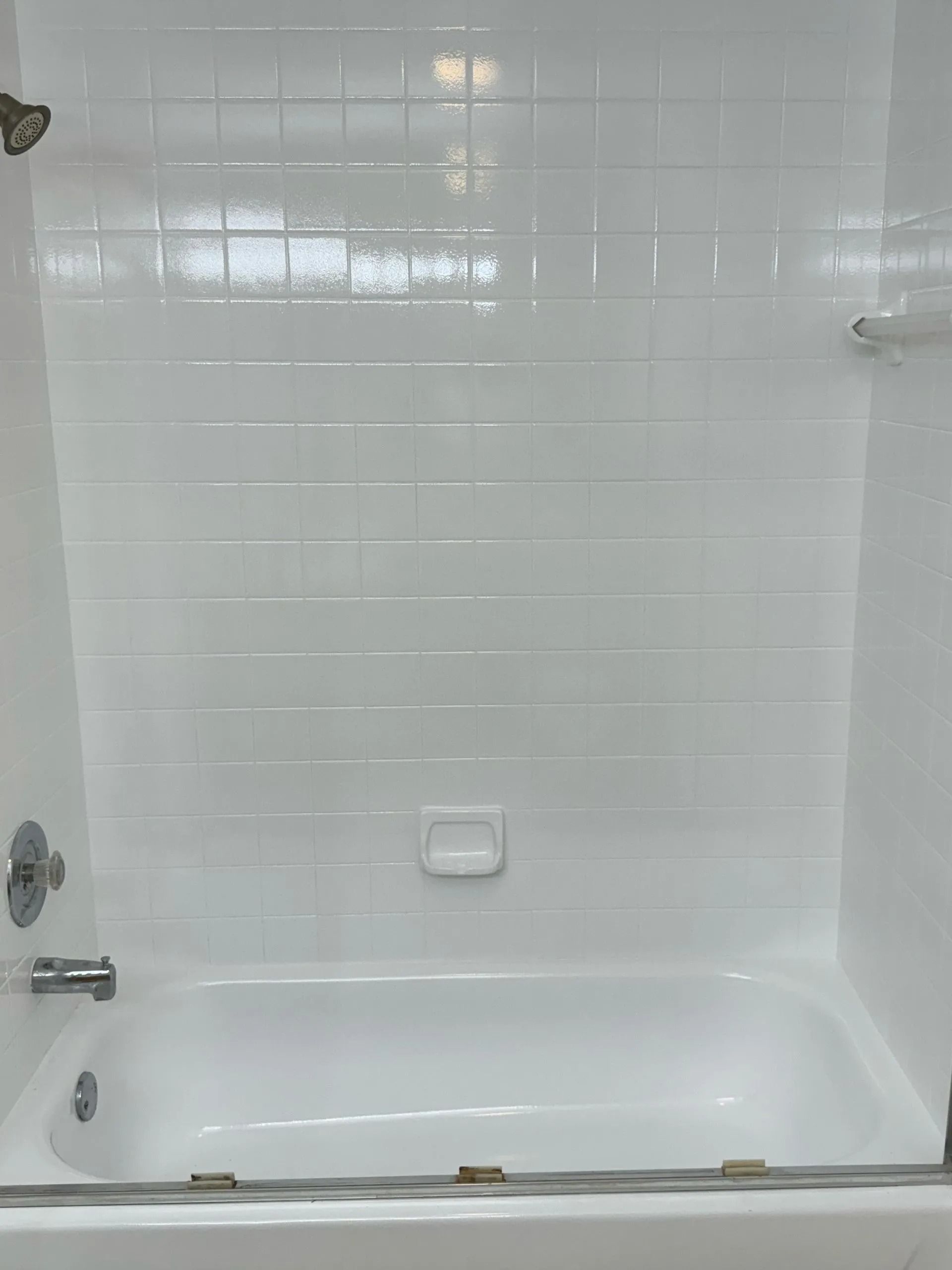 White tiled bathroom with a bathtub, shower head, and glass door.