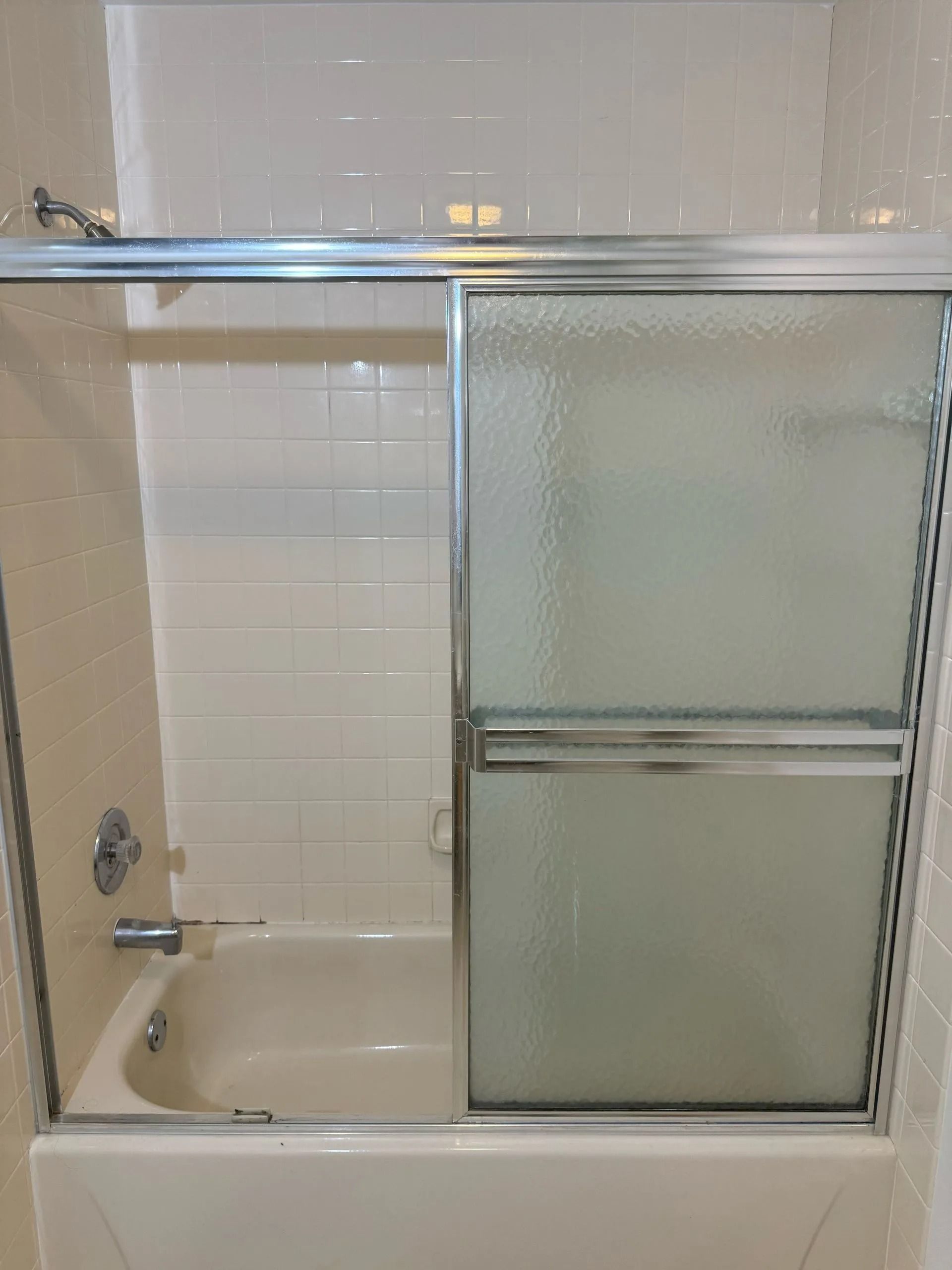 Bathtub with sliding glass shower doors. Frosted glass panel, white tile, chrome fixtures.