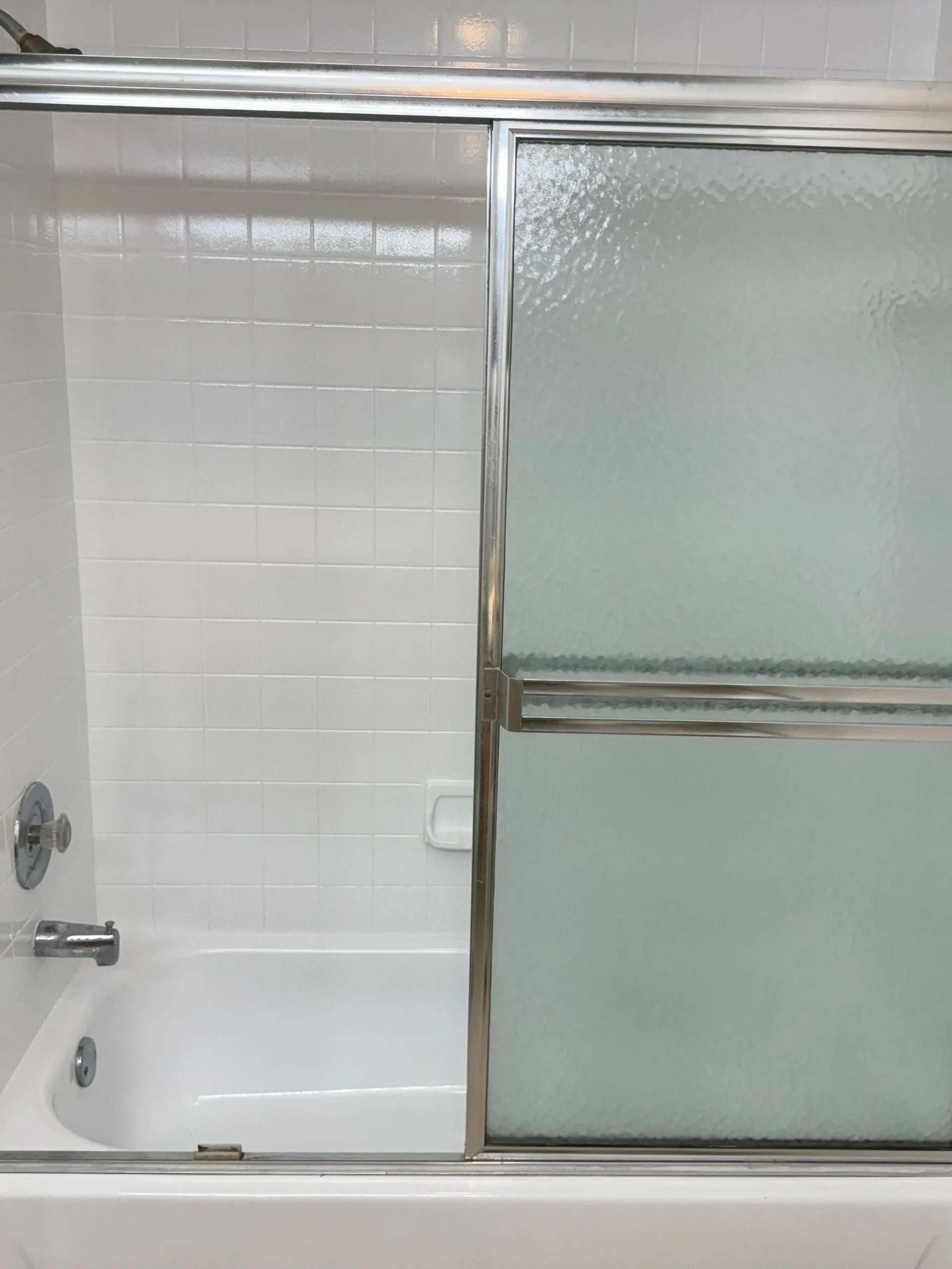 White bathtub and shower with sliding glass door, white tile walls.