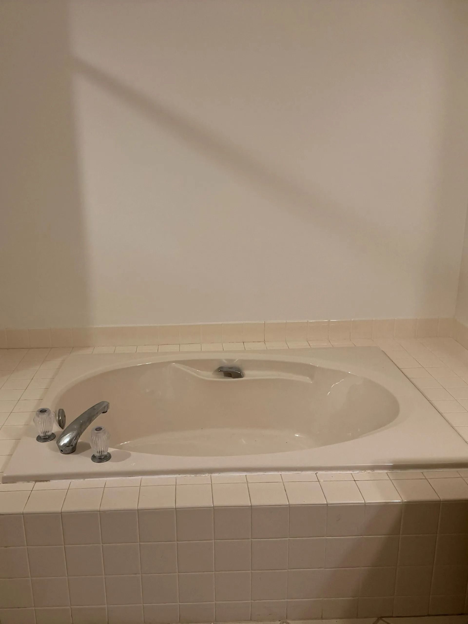A built-in, off-white bathtub with faucet and white tile surround in a bathroom.