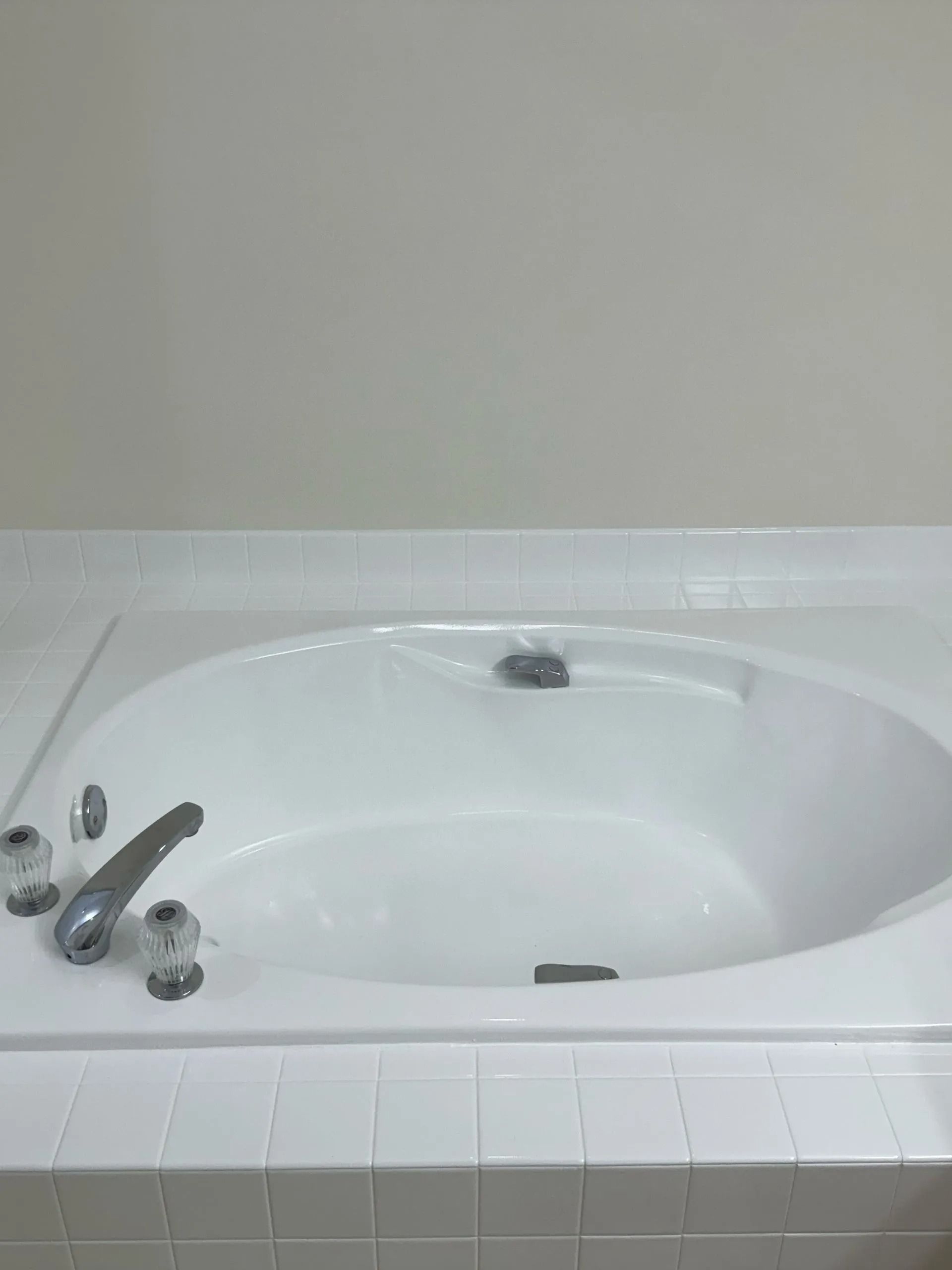 White built-in bathtub with chrome fixtures, surrounded by white tiles.