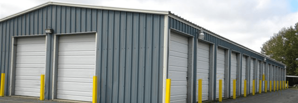 Long gray warehouse with white roll-up doors and yellow bollards along the side.