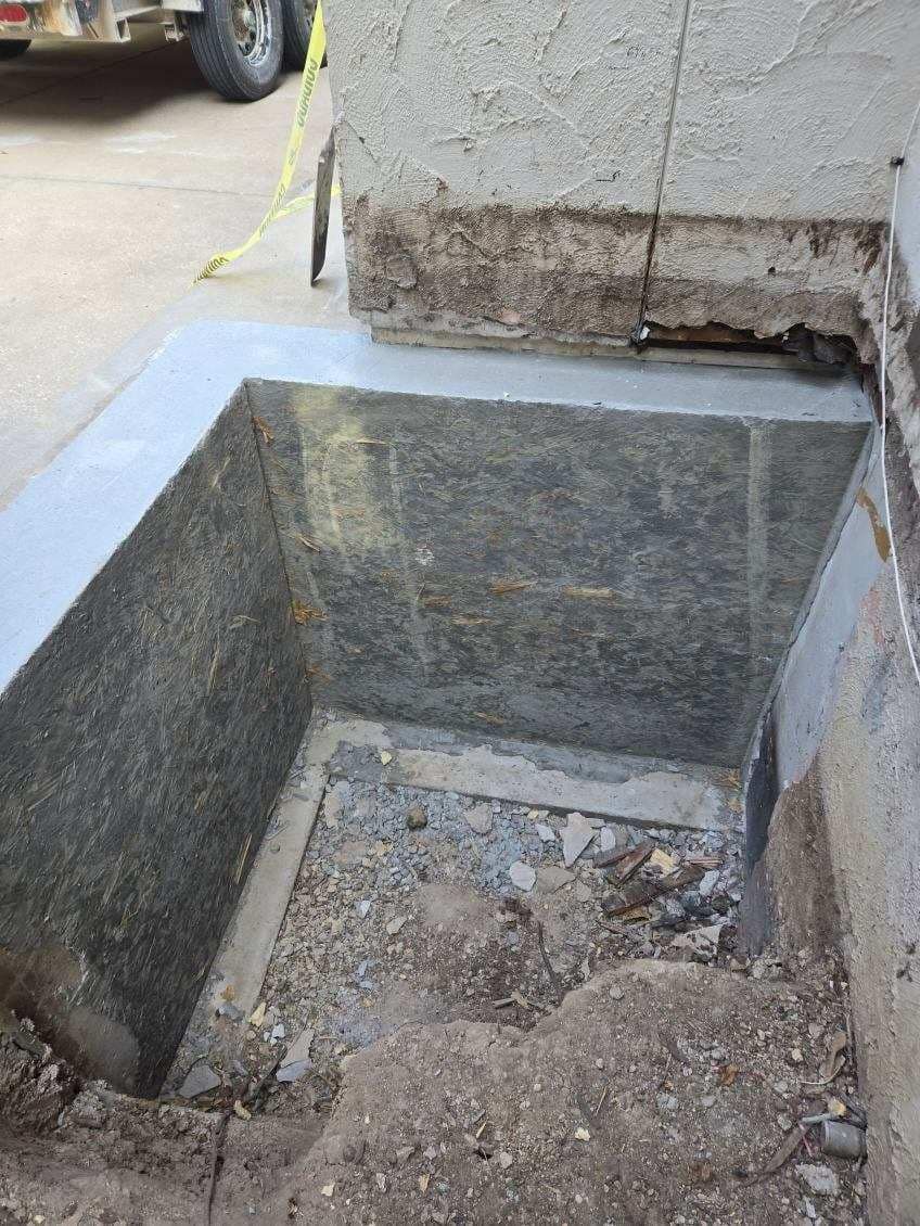 A hole in the ground next to a concrete wall with a car parked in the background.