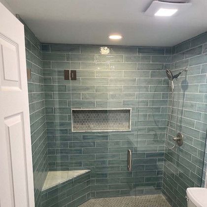 A bathroom with blue tiles and a walk in shower with a glass door.