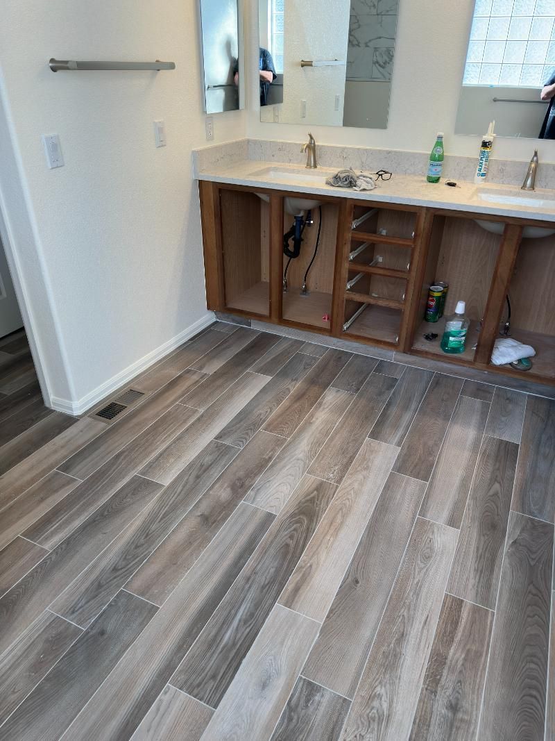 Bathroom with unfinished wooden vanity and wood-look tile flooring.