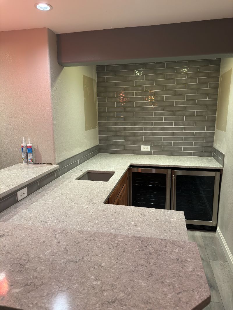 Basement bar with gray countertops, tiled backsplash, and wine fridges.