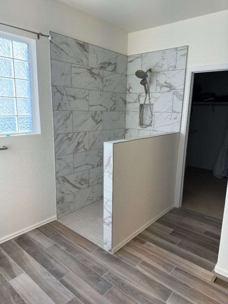 Bathroom with marble-tiled shower, white wall, and gray wood-look floor. A door leads to a closet.