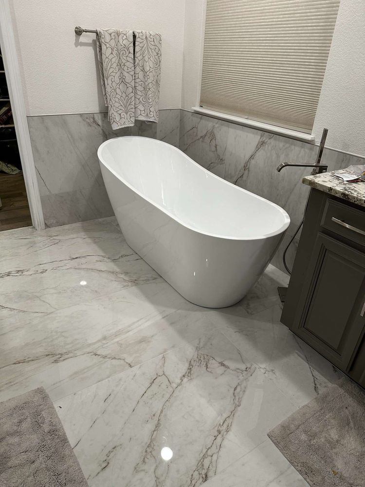 A modern bathroom with a white freestanding tub, marble-patterned tile, and gray vanity.