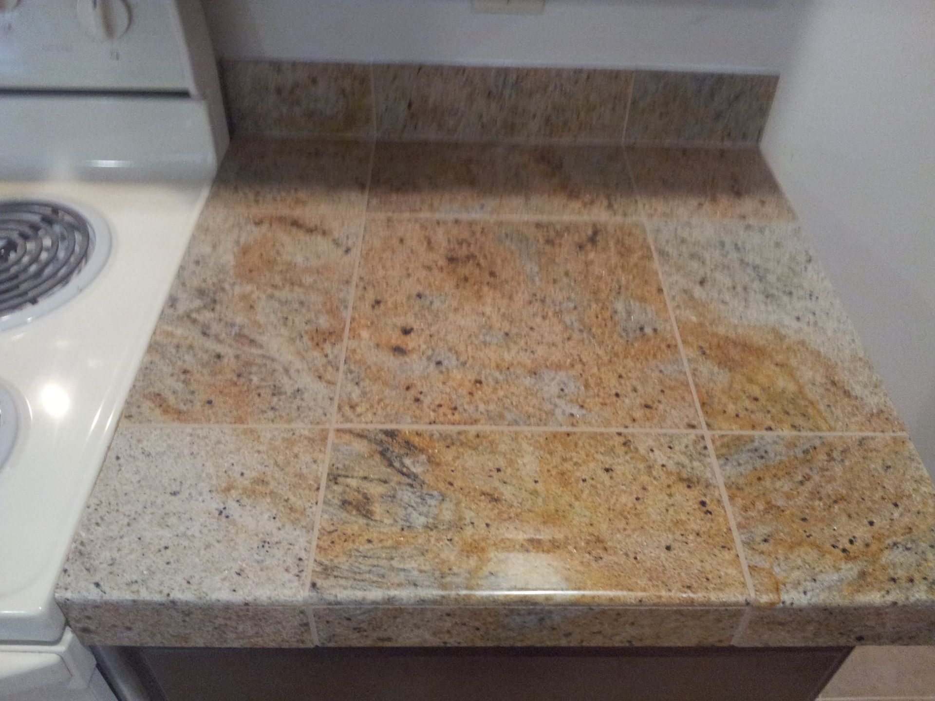 Granite tile countertop next to an electric stove. Brown, beige, and tan colors.