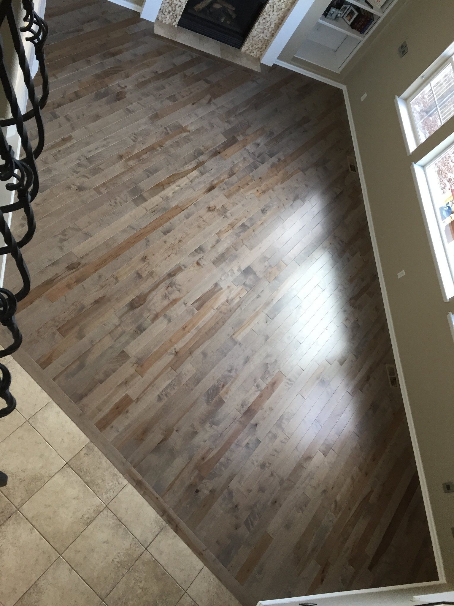 Light wood flooring laid diagonally in a room with a fireplace and windows.