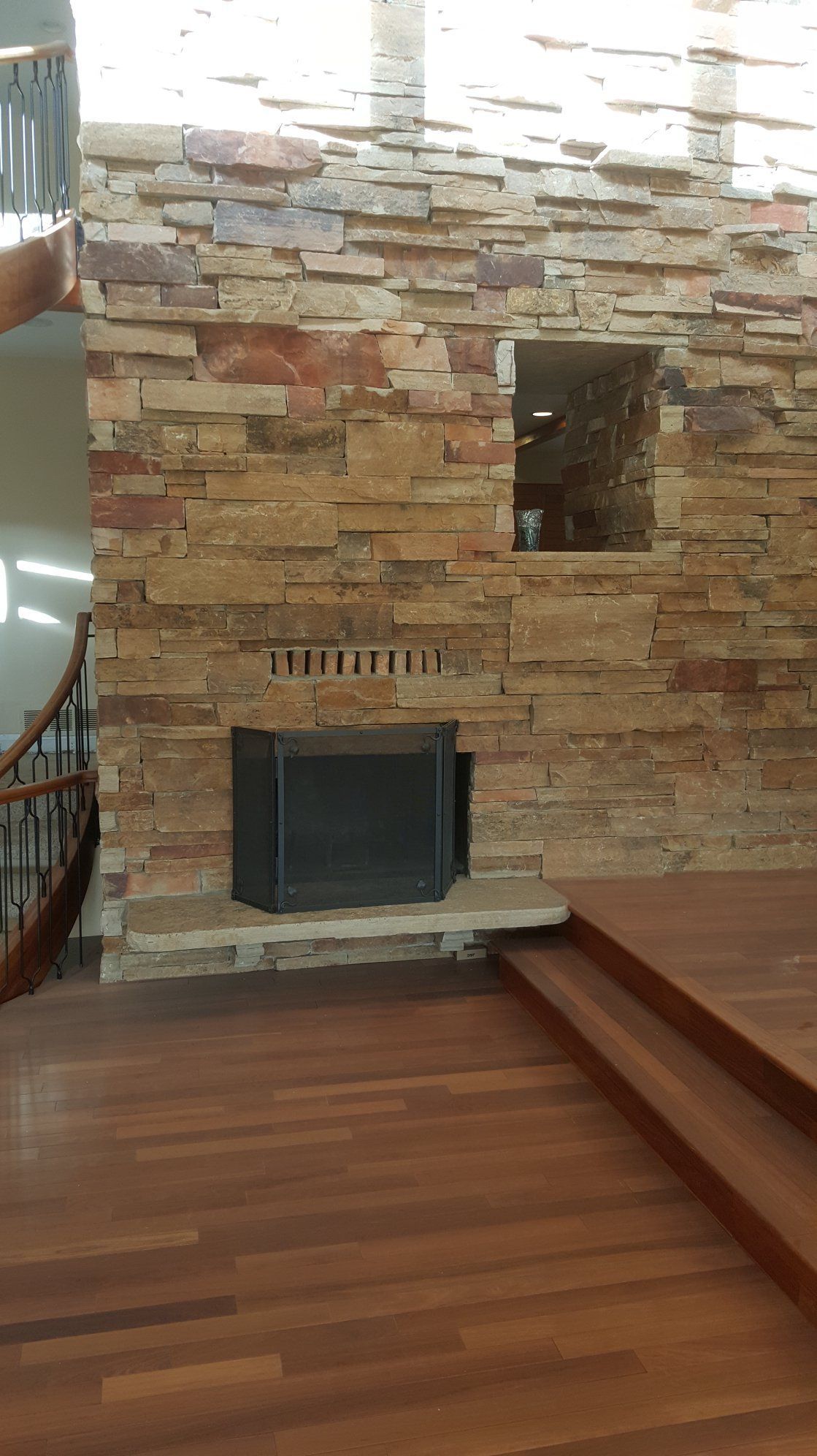 Fireplace built into a stacked stone wall with a raised wooden floor and a spiral staircase.
