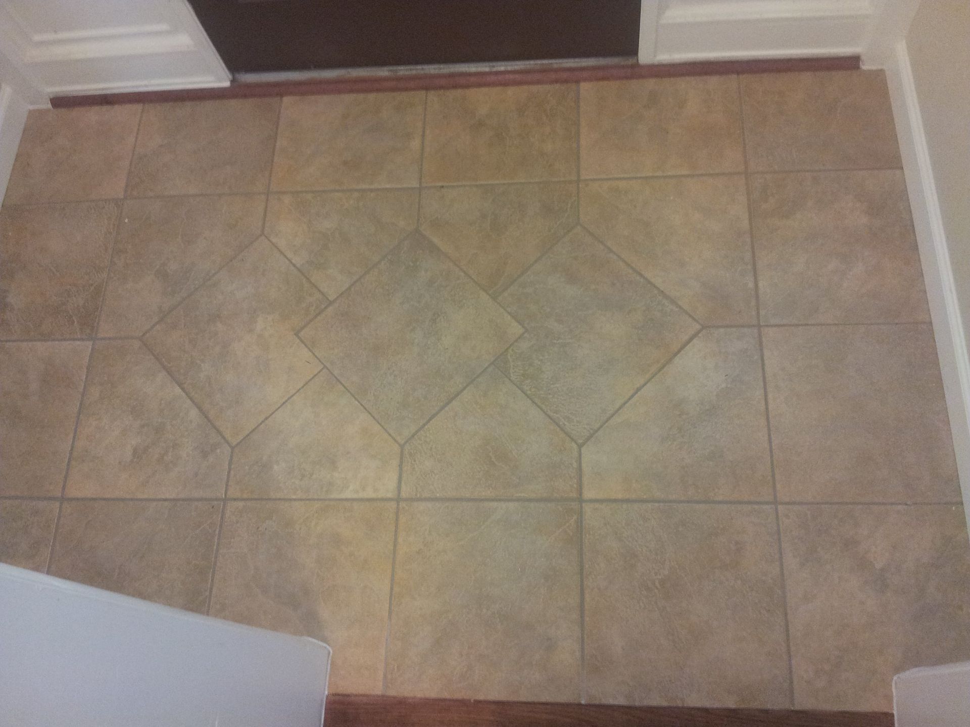 Tiled floor in a doorway; tan tiles form a central diamond pattern.